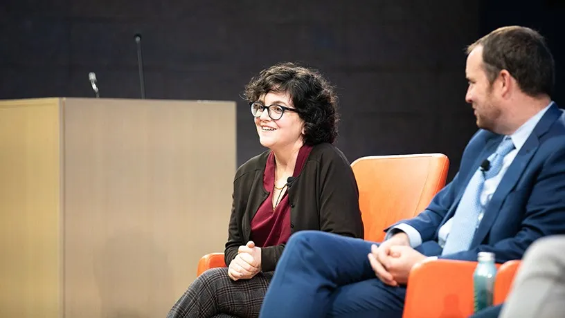 A female panelist smiling towards the audience. A male co-panelist looks at her